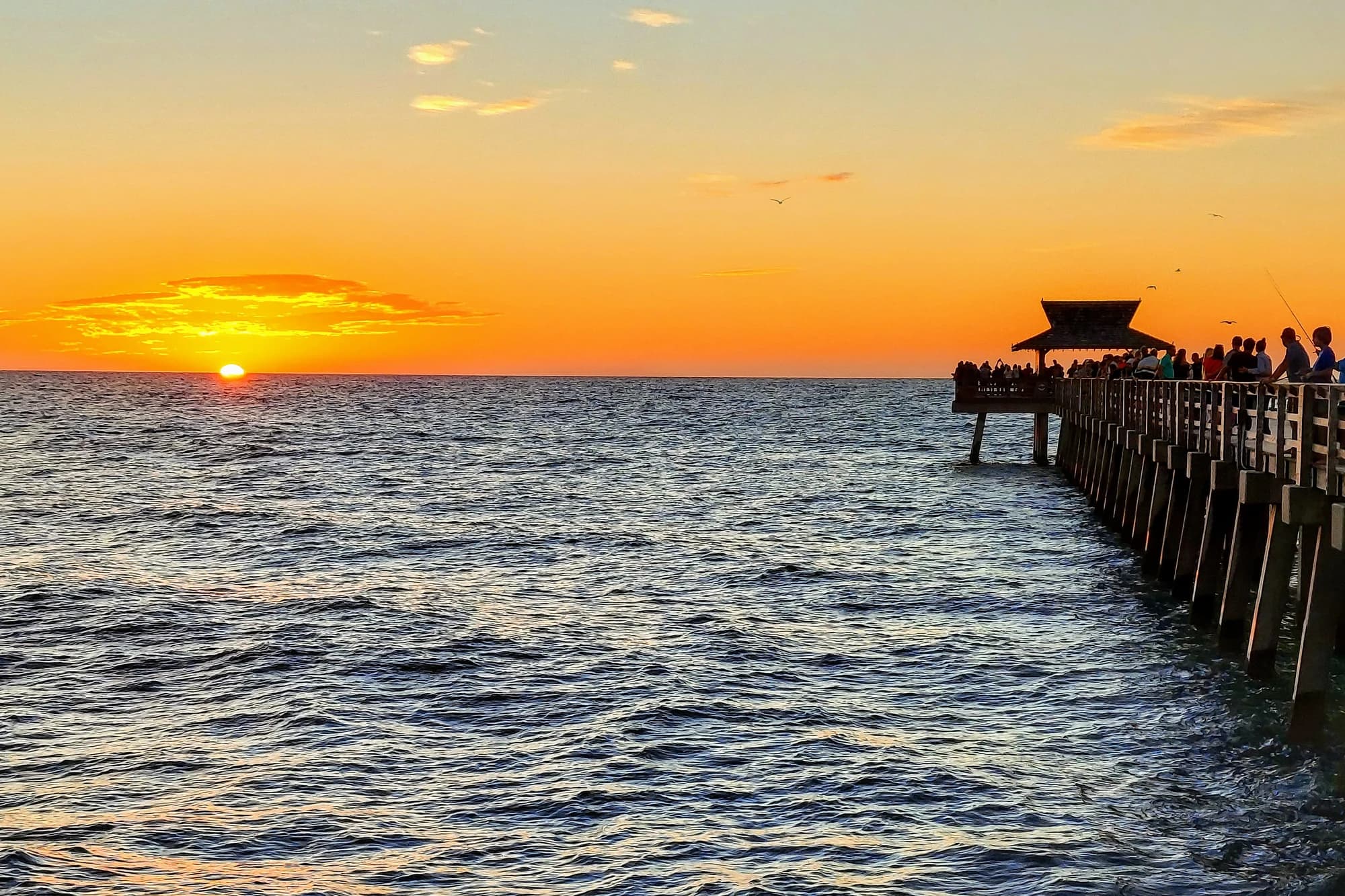 Sunset over the Gulf of Mexico at Naples Pier, Naples, Florida, with silhouetted visitors along the pier