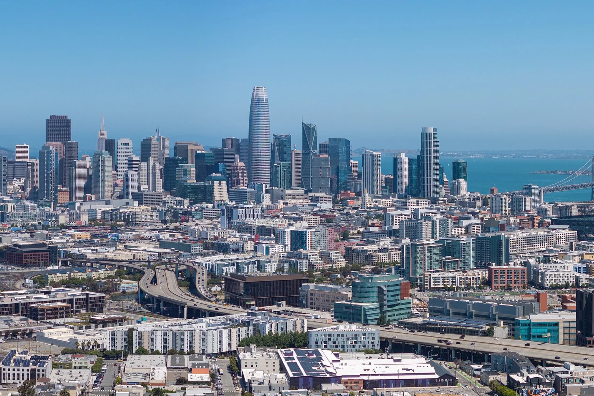 Aerial view of downtown San Francisco's skyline, including Salesforce Tower, with the Bay Bridge and San Francisco Bay in the background