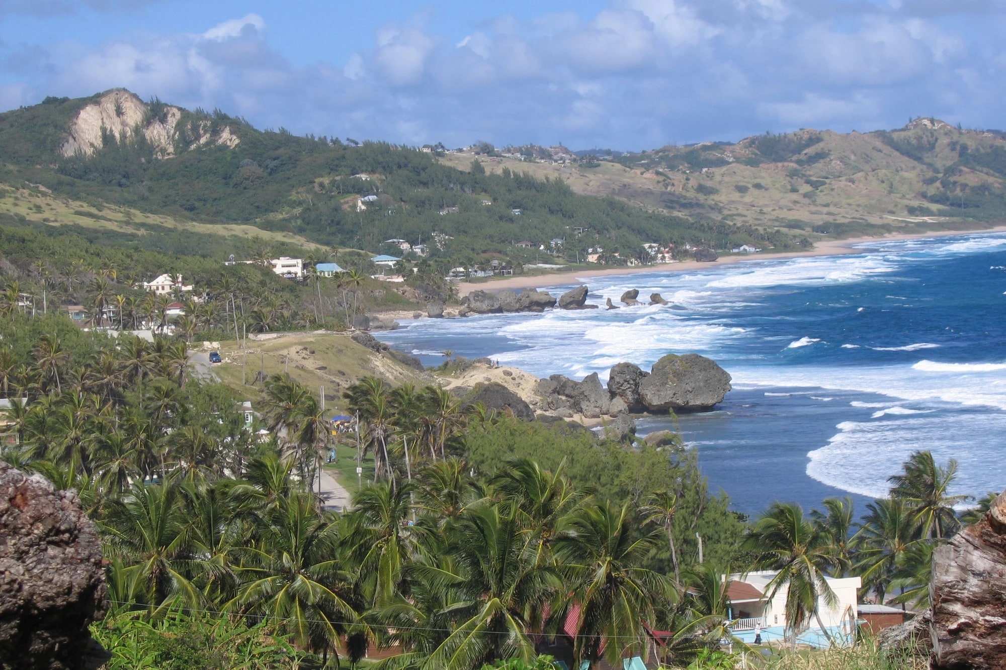 Scenic overlook of Bathsheba on Barbados' east coast, showing the Soup Bowl's large volcanic rock formations, crashing Atlantic surf, and lush green coastline