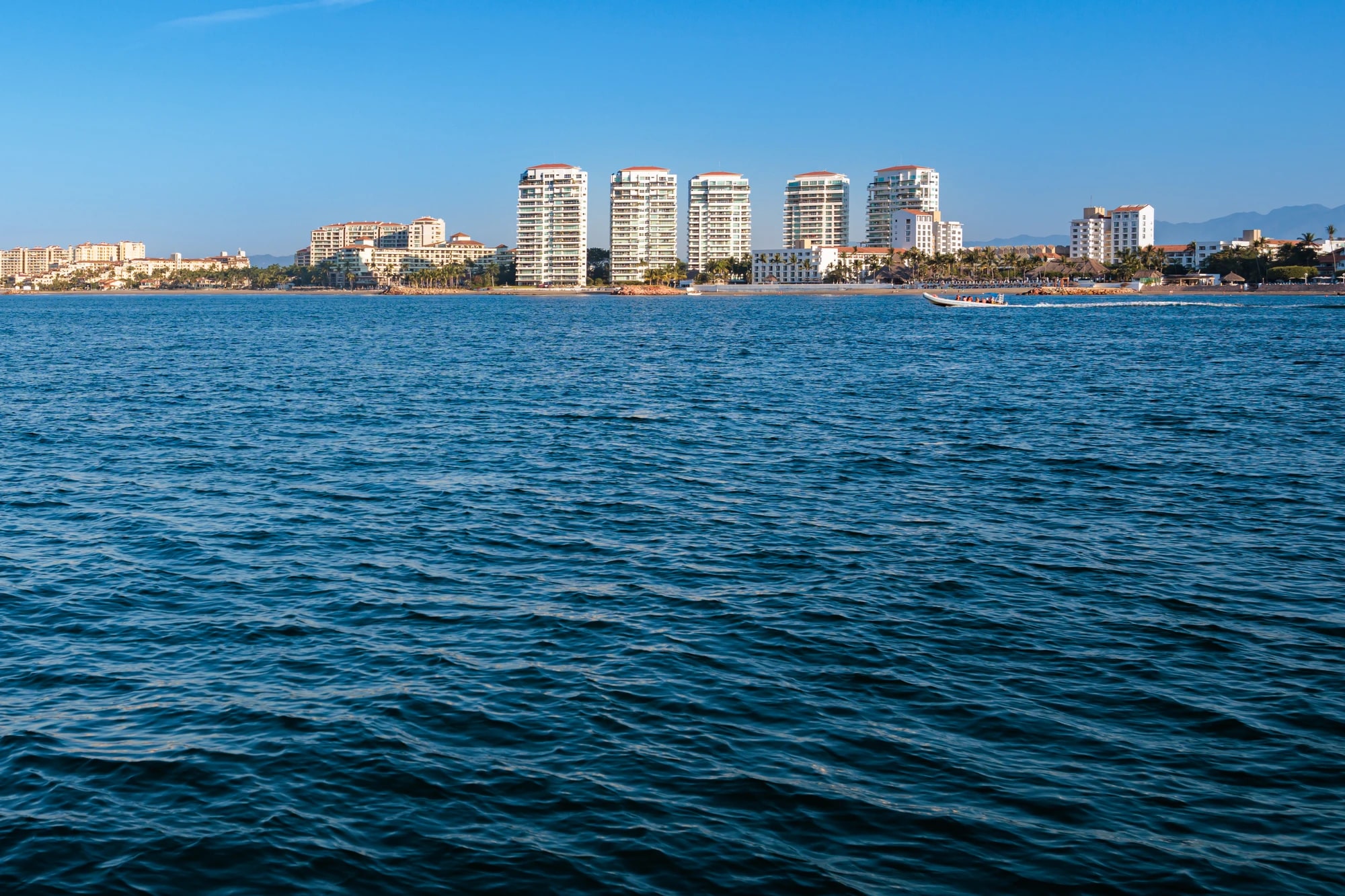 View across Banderas Bay of Puerto Vallarta's beachfront hotel towers backed by the Sierra Madre mountains under a clear blue sky