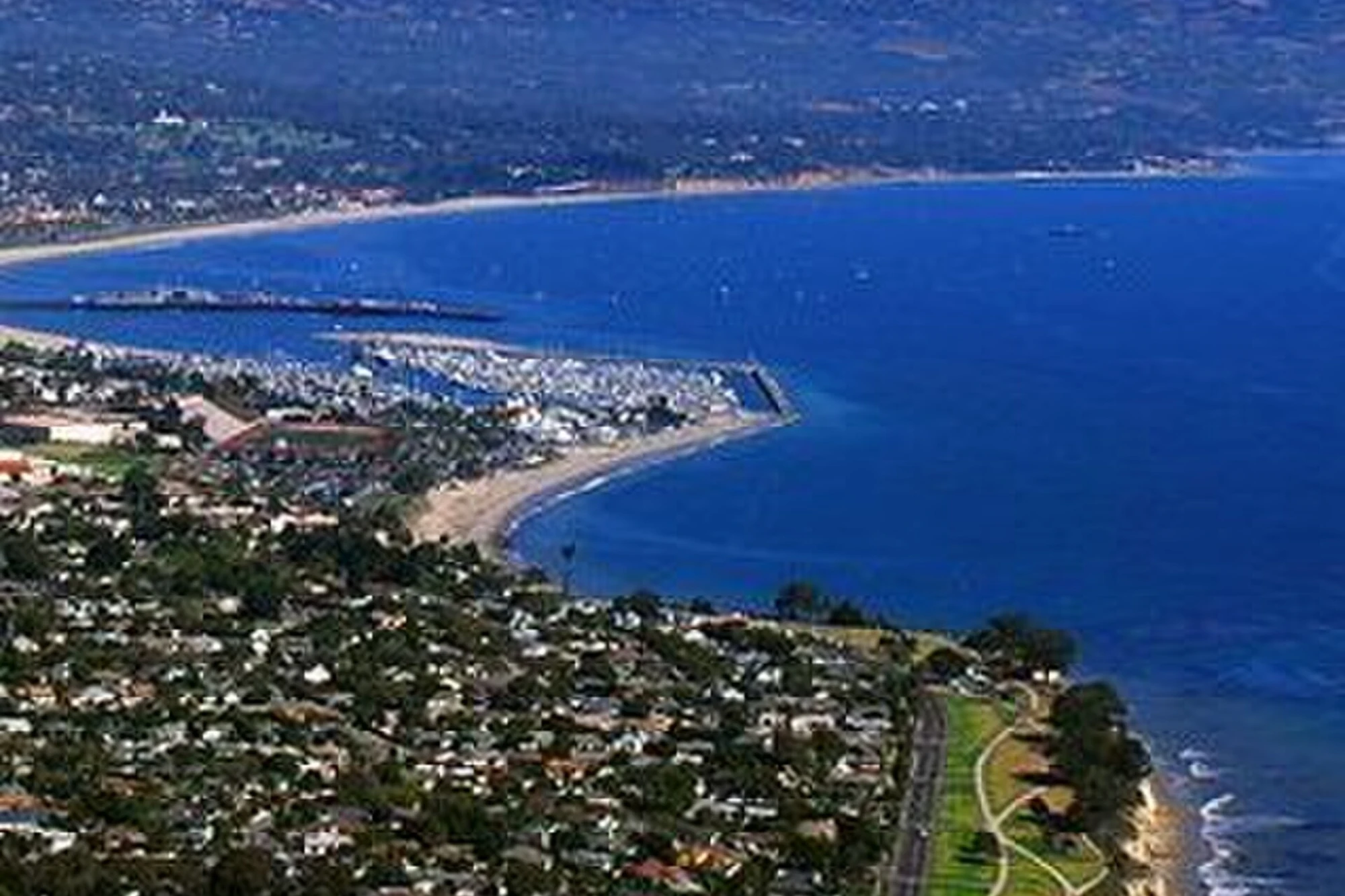 Aerial view of Santa Barbara, California, showing the coastline, marina, and Santa Ynez Mountains rising behind the city